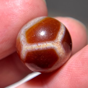 Puede incluir: Una cuenta redonda de ágata marrón con vetas blancas y un acabado brillante.