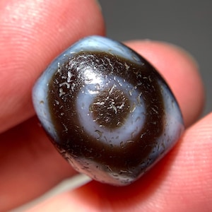 Puede incluir: Una cuenta de ágata marrón oscuro y blanca con un patrón de espiral. La cuenta es lisa y pulida.