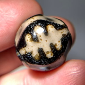 Puede incluir: Una cuenta de ágata negra y blanca con un patrón único. La cuenta es redonda y tiene una superficie lisa y pulida.