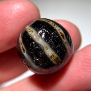 Puede incluir: Una cuenta de ágata rayada en blanco y negro con una superficie lisa y pulida.