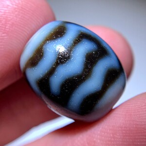 Puede incluir: Una cuenta de ágata rayada en blanco y negro con una superficie lisa y pulida.