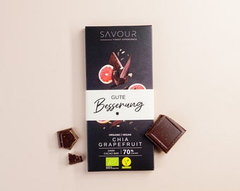 May include: A dark chocolate bar with a grapefruit and chia seed design. The bar is labeled "Gute Besserung" and "Chia Grapefruit" with a 70% cacao content. The bar is organic and vegan.