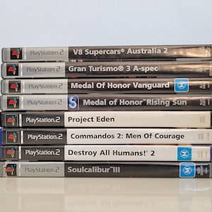 Può includere: Una pila di otto custodie di videogiochi PlayStation 2. I giochi sono: V8 Supercars Australia 2, Gran Turismo 3 A-spec, Medal of Honor Vanguard, Medal of Honor Rising Sun, Project Eden, Commandos 2: Men of Courage, Destroy All Humans! 2 e Soulcalibur III.