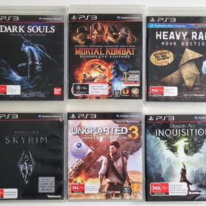 Op de afbeelding: Zes PlayStation 3-videogame-hoesjes worden getoond. Titels zijn onder meer "Dark Souls", "Mortal Kombat Komplete Edition", "Heavy Rain", "Skyrim", "Uncharted 3: Drake's Deception" en "Dragon Age: Inquisition". De hoesjes zitten in doorzichtige plastic hoesjes.