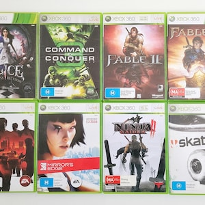 May include: A collection of ten Xbox 360 video game cases. The cases are green and black with various game titles including "Alice: Madness Returns", "Command & Conquer", "Fable II", "Fable III", "The Godfather II", "Mirror's Edge", "Ninja Gaiden", and "Skate".