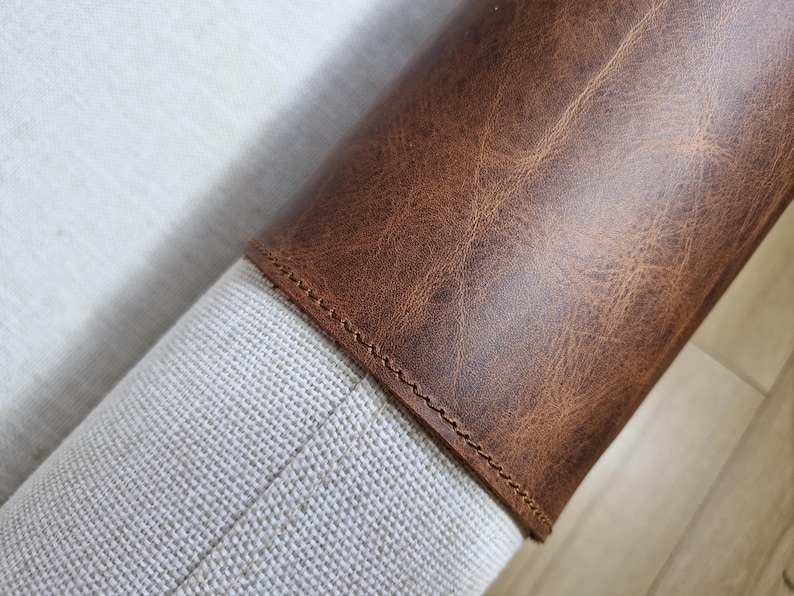May include: A cylindrical object featuring a textured, medium-brown leather wrap secured with visible stitching. The leather section is attached to a light-colored, woven fabric base that has a visible, fine-grained, off-white texture.