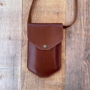 May include: A brown leather crossbody bag with a flap closure and a small pocket on the front. The bag has a brown leather strap.