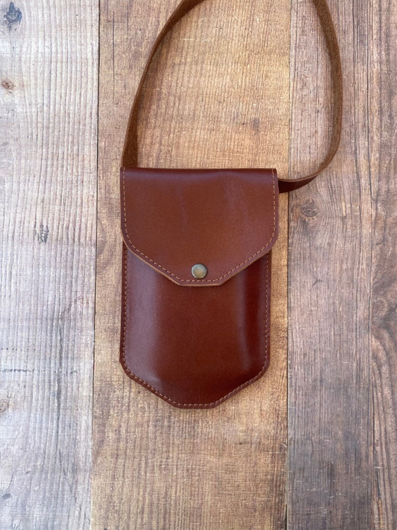 May include: A brown leather crossbody bag with a flap closure and a small pocket on the front. The bag has a brown leather strap.
