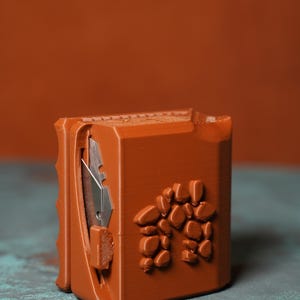 May include: A brown utility knife with a silver blade and a decorative rock design on the side. The knife is made of a 3D-printed material and has a textured surface. The knife is designed for cutting and crafting.
