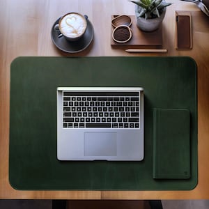 May include: A green leather desk mat with a laptop computer, a small notebook, and a cup of coffee on it.