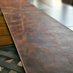 May include: A brown leather table runner with a textured surface.