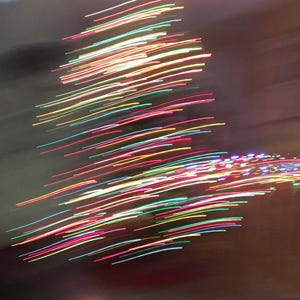 May include: Abstract image of a Christmas tree created with streaks of colorful lights. The lights are primarily red, green, yellow, and blue, creating a festive and blurred effect against a dark background.