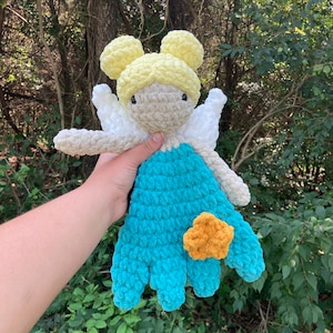 May include: A crocheted fairy doll with yellow hair, white wings, and a turquoise dress. The doll has a yellow flower on its dress.