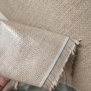 May include: Close-up of a beige burlap fabric with a white trim and frayed edges. The fabric has a woven texture.