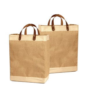 May include: Two brown burlap tote bags with leather handles and a cream colored trim. The bags are empty and sitting on a white background.