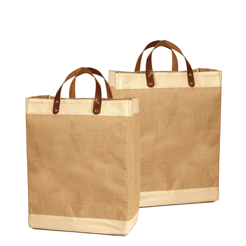 May include: Two brown burlap tote bags with leather handles and a cream colored trim. The bags are empty and sitting on a white background.