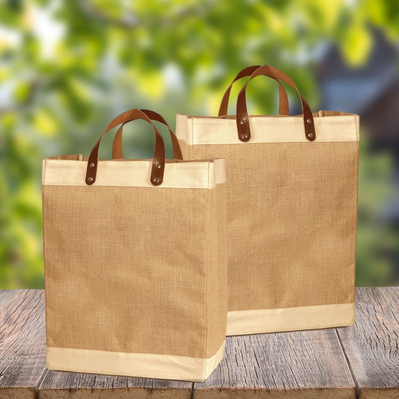 May include: Two brown burlap tote bags with leather handles and a white trim. The bags are sitting on a wooden surface.