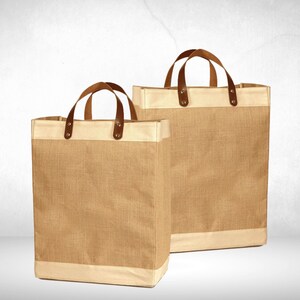 May include: Two brown burlap tote bags with leather handles and a white trim. The bags are empty and sitting on a white surface.