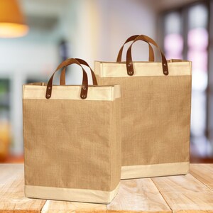 May include: Two brown burlap tote bags with leather handles. The bags have a cream colored trim around the top.
