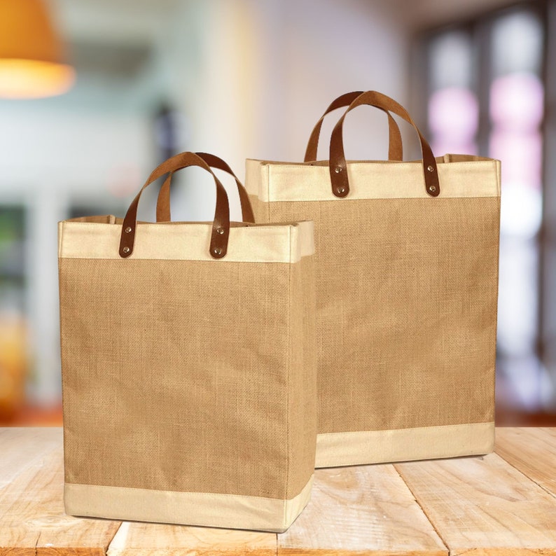 May include: Two brown burlap tote bags with leather handles. The bags have a cream colored trim around the top.