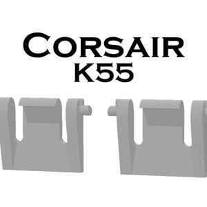 May include: Two gray plastic components with a unique shape, possibly for a keyboard or electronic device. The text "CORSAIR K55" is displayed in black above the components, indicating a product name or model.