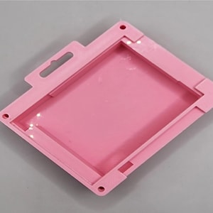Puede incluir: Una caja de plástico rosa con una abertura rectangular. La caja tiene una pequeña manija en la parte superior.