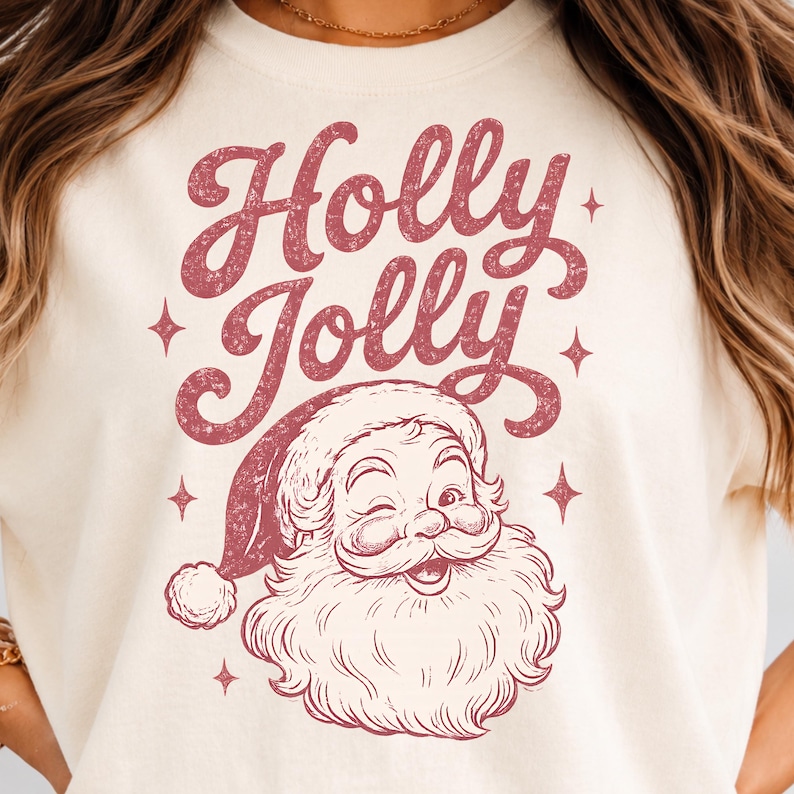 May include: A cream-colored t-shirt featuring a distressed red graphic of a winking Santa Claus wearing a hat. Above the Santa illustration, the text "Holly Jolly" is printed in a bold, cursive, distressed red font, surrounded by small stars.