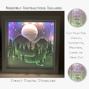 Puede incluir: Un marco blanco con una escena de papel recortado iluminada que representa una luna, montañas y árboles. La escena está iluminada con luces de colores. El texto "ASSEMBLY INSTRUCTIONS INCLUDED" y "DIRECT DIGITAL DOWNLOAD" es visible. El texto "CUT FILES FOR CRICUT, SILHOUETTE, BROTHER, LASER OR HAND CUT" también es visible.