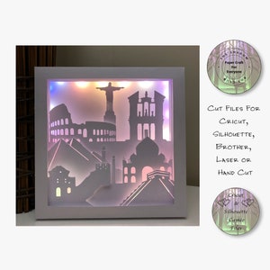 Könnte beinhalten: Eine weiße Leuchtbox mit einer mehrfarbigen LED-Lichtquelle. Die Box zeigt eine Silhouette berühmter Sehenswürdigkeiten aus aller Welt, darunter das Kolosseum, das Taj Mahal und die Große Pyramide von Gizeh. Der Text "CUT FILES FOR CRICUT, SILHOUETTE, BROTHER, LASER OR HAND CUT" ist unterhalb der Box sichtbar.