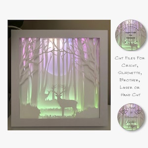 Puede incluir: Una caja de sombra de papel blanco con una escena de bosque y dos siluetas de ciervos. La caja está iluminada desde atrás con una luz multicolor, creando un efecto brillante. El texto "CUT FILES FOR CRICUT, SILHOUETTE, BROTHER, LASER OR HAND CUT" es visible en el lado derecho de la imagen. El texto "Cricut & Silhouette Cameo Files" es visible en un círculo en la parte inferior derecha.