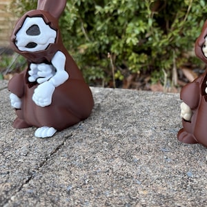 Può includere: Due statuine di coniglio in ceramica marrone con scheletri dipinti di bianco all'interno. I conigli sono seduti su una superficie di cemento grigia.