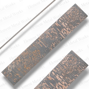 May include: A rectangular metal billet featuring a layered mokume gane pattern with alternating dark gray and copper-colored wavy lines. The surface displays a distinct organic, wood-grain-like texture throughout the entire length of the material.