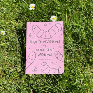 Peut inclure: Un livret rose rectangulaire avec des illustrations au trait noir représentant quatre vers souriants. Le texte indique : EARTHWORMS vs. COMPOST WORMS tiny guys, big jobs. La couverture présente de petites feuilles et des cercles.