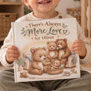 Peut inclure: Un livre pour enfants à couverture rigide intitulé There's Always More Love for Oliver, illustré de trois ours bruns et d'un ourson dans un panier sur un canapé, avec un petit train en bois et des chaussons de bébé au sol.