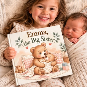 Puede incluir: Un libro cuadrado de tapa dura titulado Emma, the Big Sister. La portada muestra un oso pardo sosteniendo a un osezno, ambos envueltos en una manta. La ilustración incluye un tren de juguete de madera, cojines de cuadros rosas y pequeños corazones rojos.