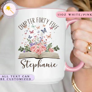 May include: White ceramic mug with a pink interior and handle. The mug features the text "CHAPTER FORTY FIVE" and "Stephanie" with a floral and butterfly design. The mug is 15 oz.