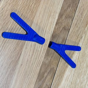May include: Two identical blue Y-shaped components with a textured surface finish. Each piece features two elongated arms extending from a central cylindrical base. The objects are positioned at an angle, displaying a consistent matte blue colour.