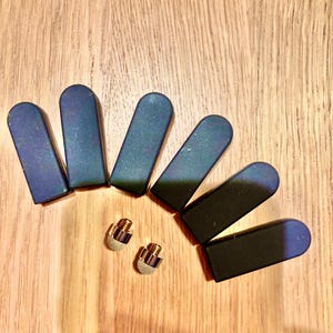 May include: A collection of six dark blue and black stylus tips with a metallic sheen, arranged on a wooden surface. Two small, silver and gold stylus tips are also present. The tips are designed for use with touch screen devices.