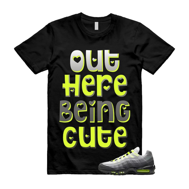 May include: Black t-shirt with the text "OUT Here Being Cute" in a playful font with heart accents. A pair of gray and black sneakers with neon green accents is placed at the bottom right.