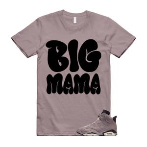 May include: A mauve t-shirt with the words "BIG MAMA" in large, black, bubble letters. A pair of grey and white trainers is at the bottom of the shirt.