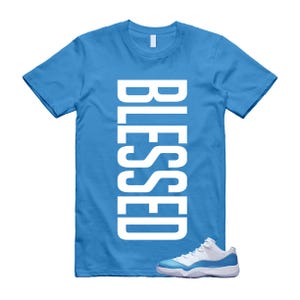 Puede incluir: Una camiseta azul claro con la palabra "BLESSED" impresa verticalmente en blanco. Un par de zapatillas blancas y azul claro se encuentra en la parte inferior de la camiseta.