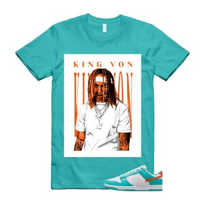 May include: A turquoise t-shirt with a graphic of King Von and the text "KING VON". The graphic is in a white rectangle with orange vertical lines. White, turquoise, and orange sneakers are at the bottom.