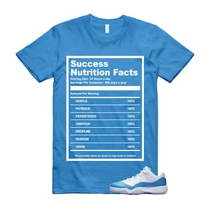 Puede incluir: Camiseta azul claro con el texto "Success Nutrition Facts" en un recuadro blanco. El gr&aacute;fico enumera "Hustle", "Patience", "Persistence", "Ambition", "Discipline", "Passion" y "Grind" al 100%. Una zapatilla blanca y azul en la parte inferior.