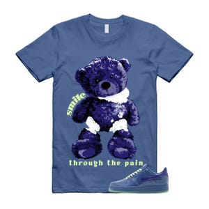 May include: Blue t-shirt featuring a purple teddy bear graphic with the words "smile through the pain" in light green. A pair of blue sneakers with a purple swoosh are at the bottom of the image.