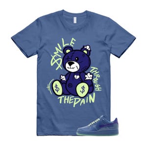 May include: A blue t-shirt with a graphic of a purple teddy bear with dollar signs and the words "SMILE THROUGH THE PAIN" in green. A blue sneaker with a purple swoosh is at the bottom.