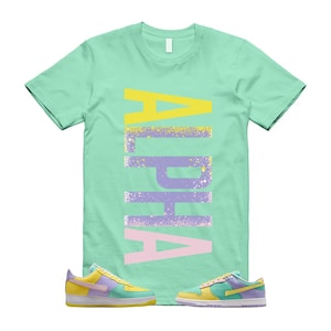 May include: A mint green t-shirt with the word "ALPHA" in a vertical design, using yellow, purple, and pink colors. The shirt is paired with two pairs of colorful sneakers, featuring yellow, purple, and blue hues.