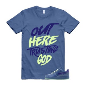 May include: A blue t-shirt with the text "OUT HERE TRUSTING GOD" in a mix of blue and green lettering. A blue sneaker with a purple accent is placed below the shirt.