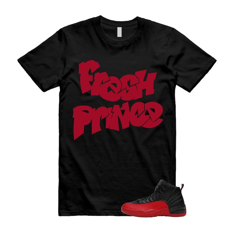 May include: Black t-shirt with the words "Fresh Prince" in red graffiti-style lettering. A pair of black and red sneakers is at the bottom of the image. The t-shirt is a crew neck style.