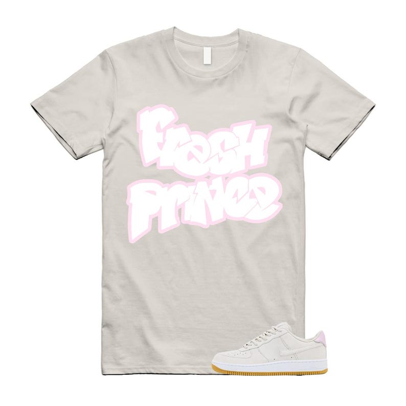 May include: A light beige t-shirt with the words "Fresh Prince" in white with a pink outline. A pair of light beige sneakers with a white sole and a gum-colored outsole are at the bottom of the image.