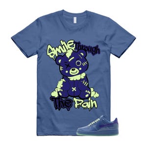 May include: A blue t-shirt with a graphic of a purple teddy bear with stitches and the words "Smile Through The Pain" in a neon green font. A pair of blue sneakers with a purple swoosh are at the bottom.